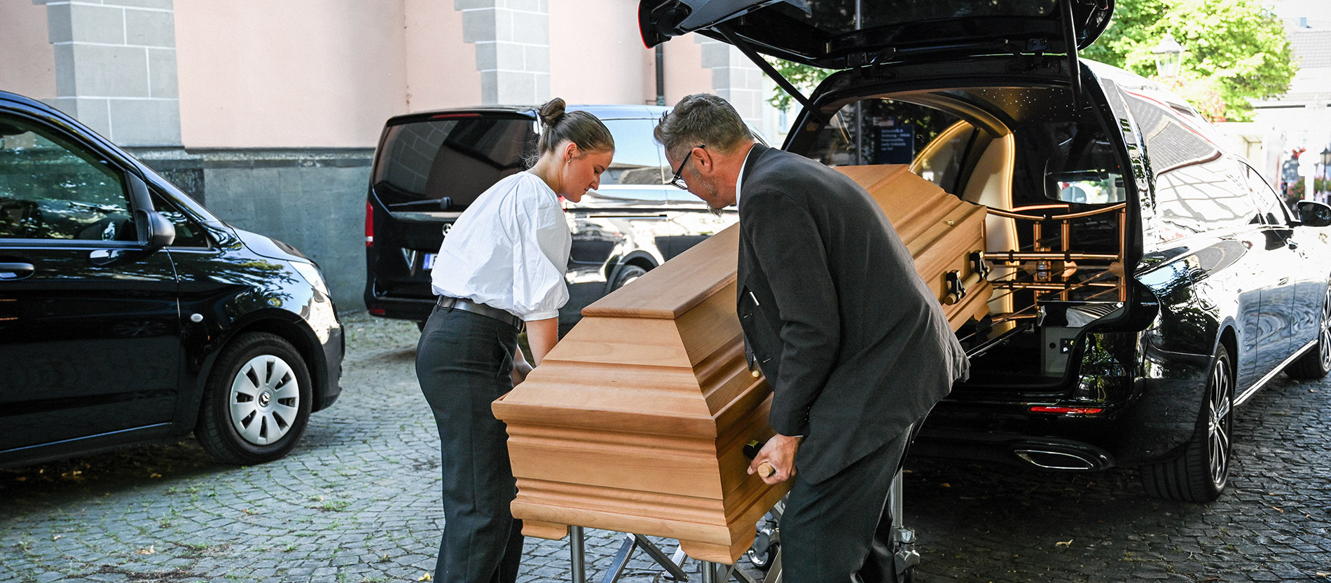 Mitarbeiter einer Bestattungsfirma heben einen Sarg aus dem Leichenwagen vor der Totenmesse in einer Kirche in Bad Honnef.