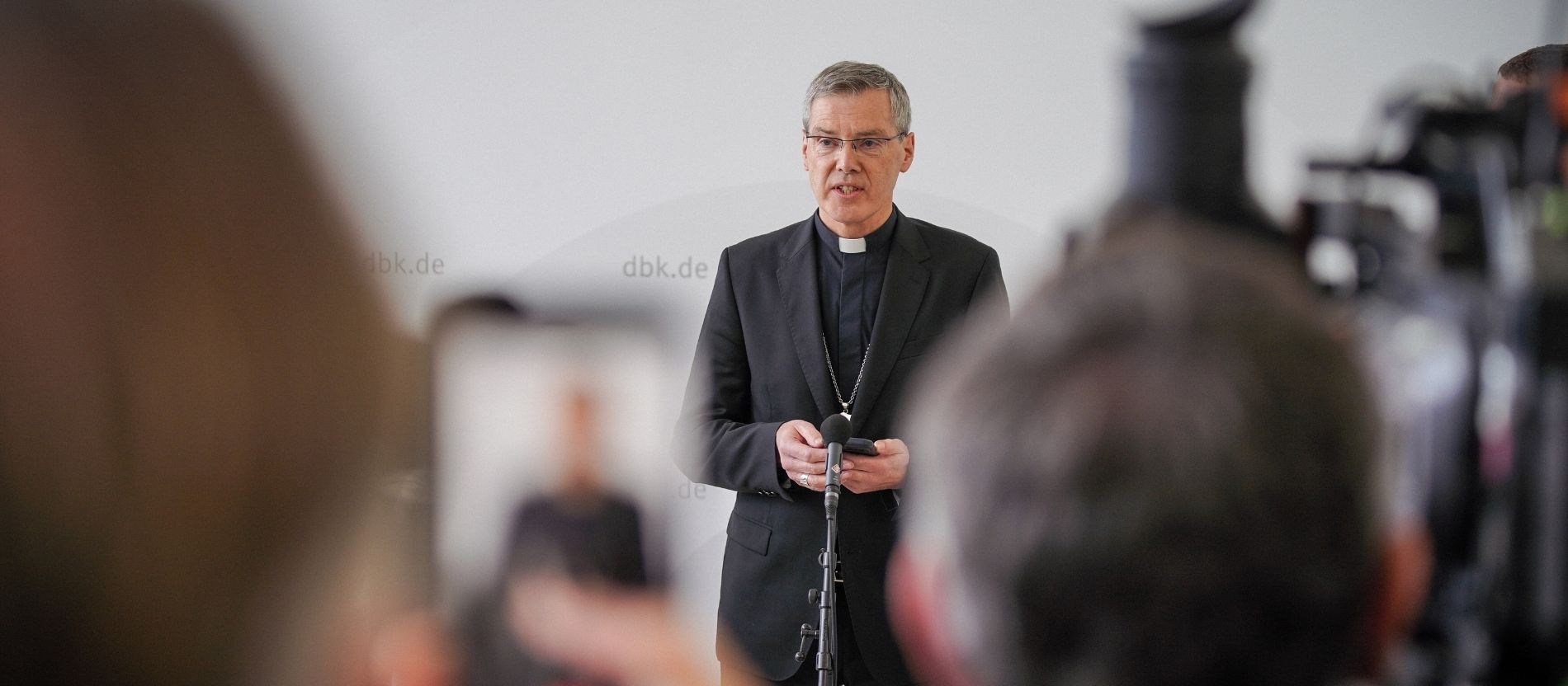 Bischof Heiner Wilmer spricht bei einer Pressekonferenz, im Vordergrund sind unscharf Fernsehkameras zu sehen