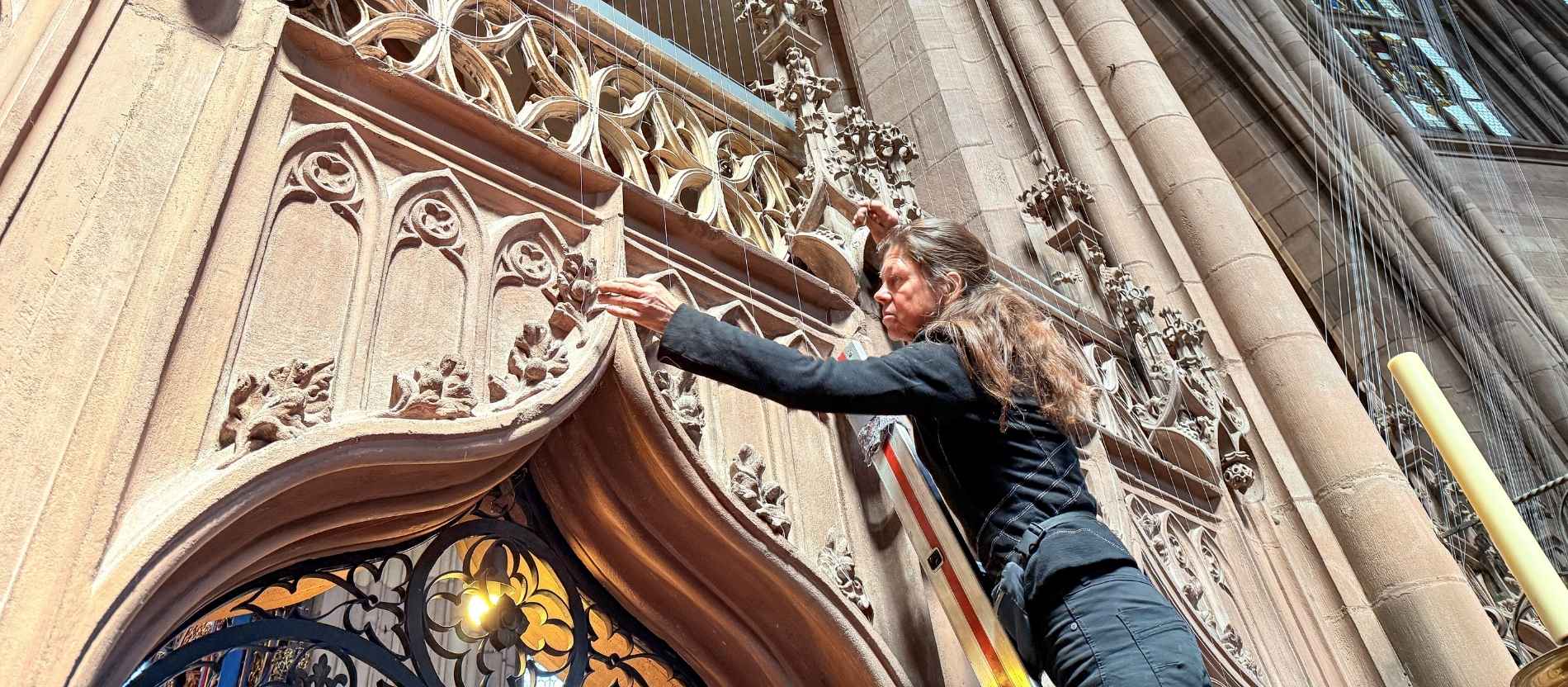 Die Künstlerin steht auf einer Leiter und berührt die dünnen Fäden, die in der Kirche hängen. 