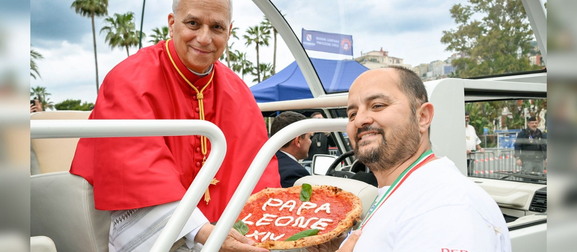 Ein Mann übergibt dem Papst eine Pizza, auf der mit Käse 