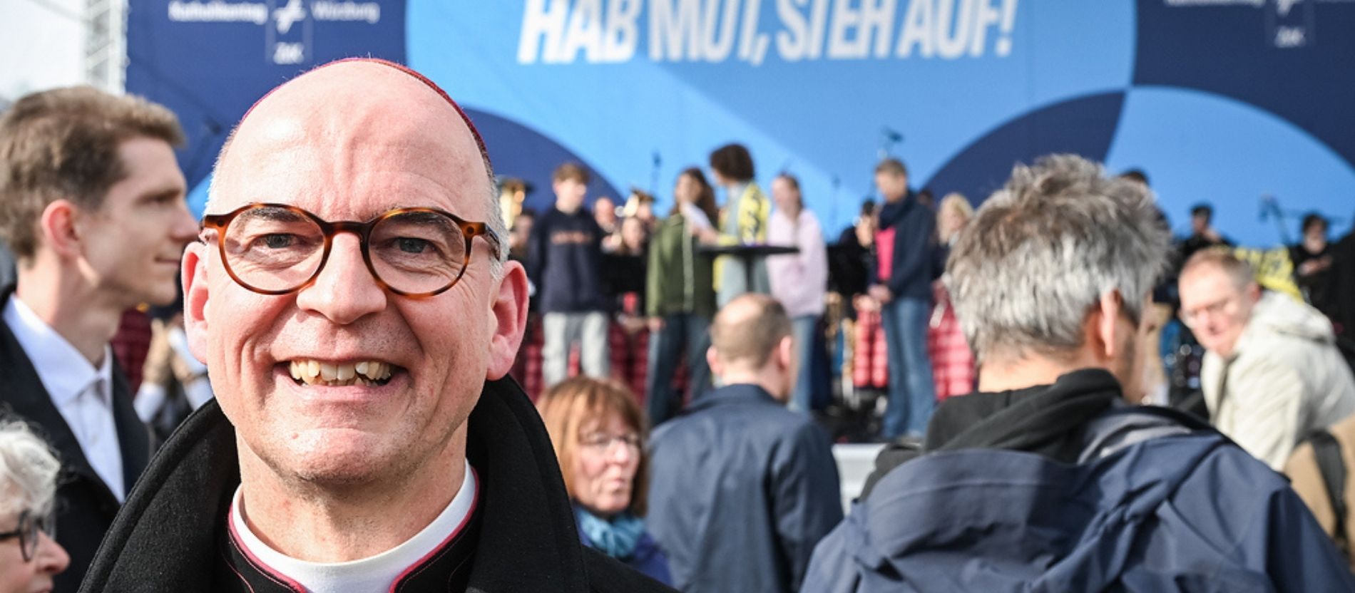 Franz Jung, Bischof von Würzburg, hinter ihm andere Teilnehmer und die Bühne mit dem Leitwort "Hab Mut, steh auf!", bei der Eröffnung des 104. Katholikentags.