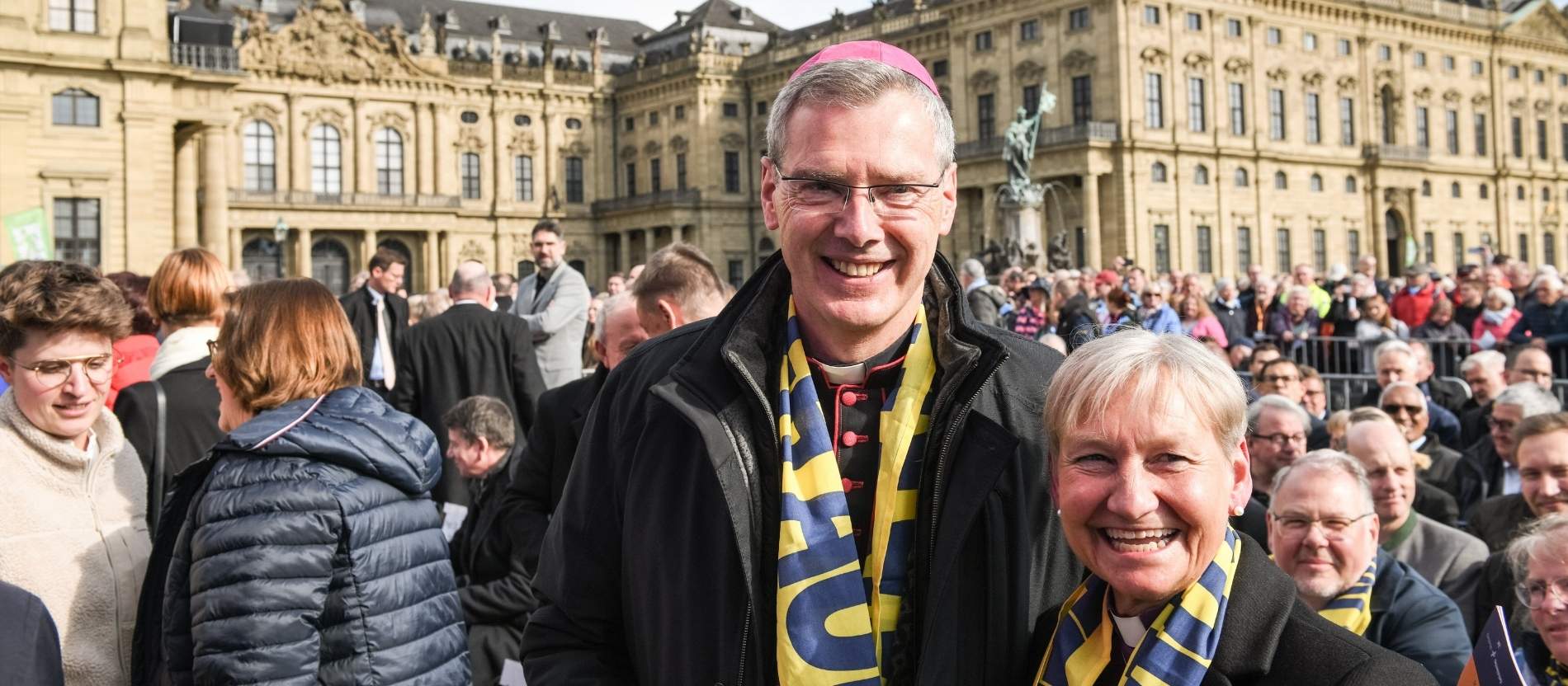 Bischof Heiner Wilmer und Bischöfin Kirsten Fehrs posieren für ein Foto, im Hintergrund eine Menschenmenge beim Katholikentag