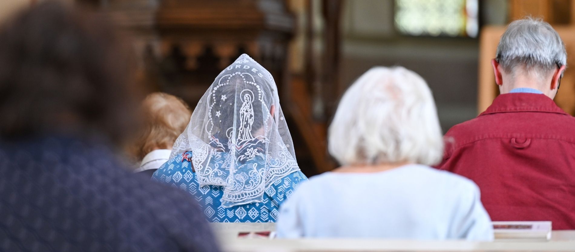 Rückansicht auf fünf Gottesdienstbesucher, eine Frau in der Mitte trägt ein weißes Kopftuch. 