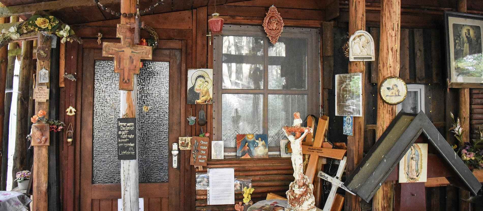 An der Fassade einer Holzhütte hängen zahlreiche Devotionalien in der Einsiedelei Mariental