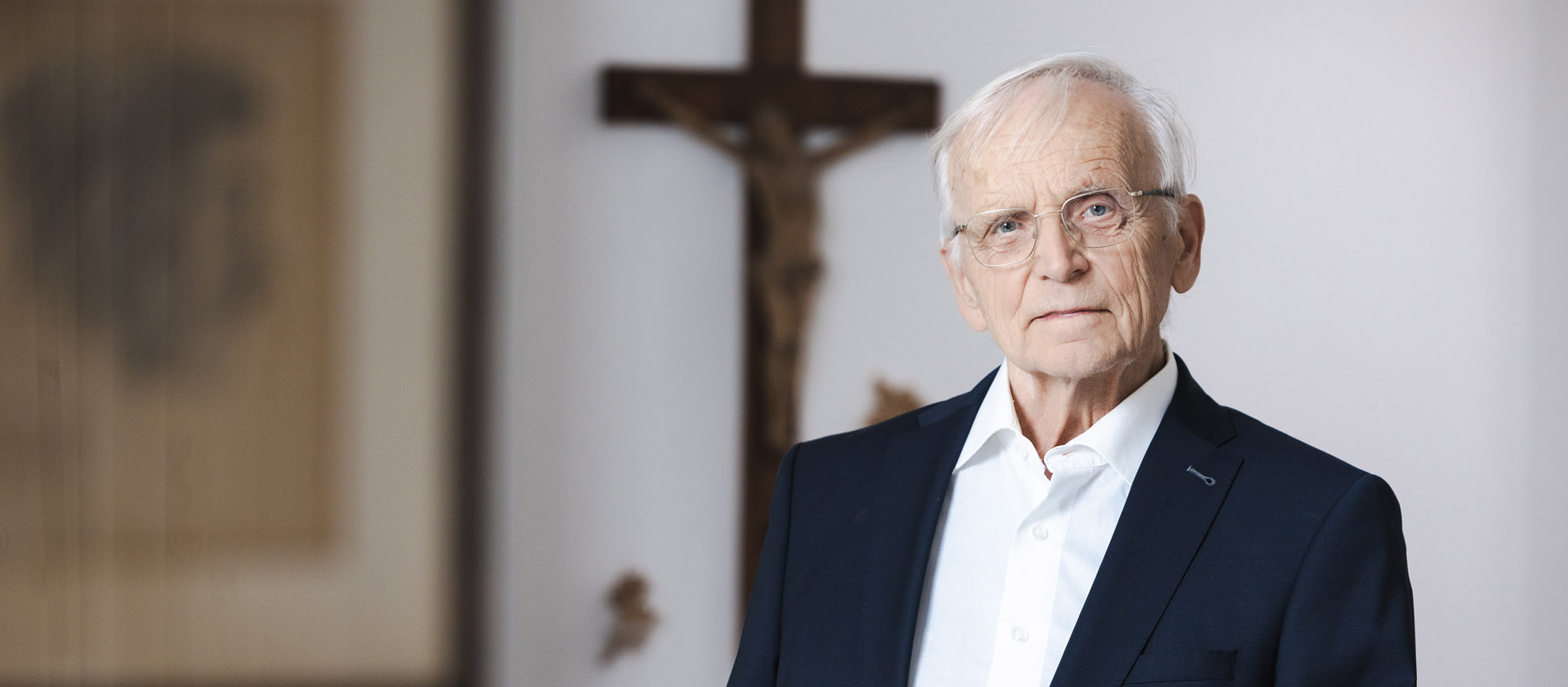 Der Pastoraltheologe Paul Zulehner schaut neutral in die Kamera. Im Hintergrund hängt ein Kreuz an der Wand.