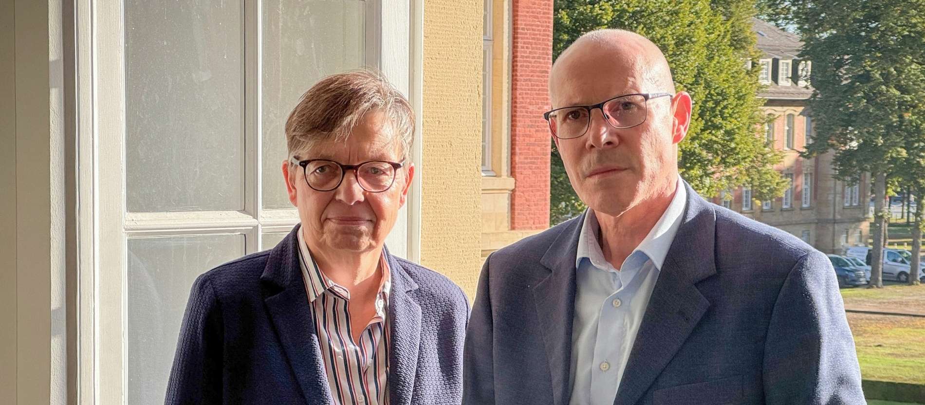 Die Autoren der Studie zu Geistlichen Missbrauch, Judith Könemann und Thomas Frings, stehen vor einem geöffneten Fenster