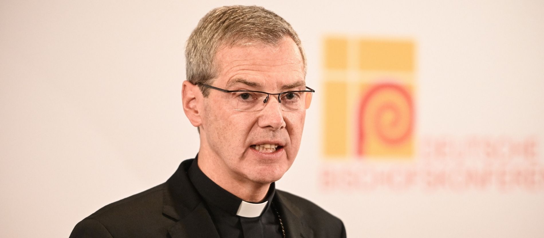 Bischof Heiner Wilmer spricht bei einer Pressekonferenz, im Hintergrund das Logo der Deutschen Bischofskonferenz