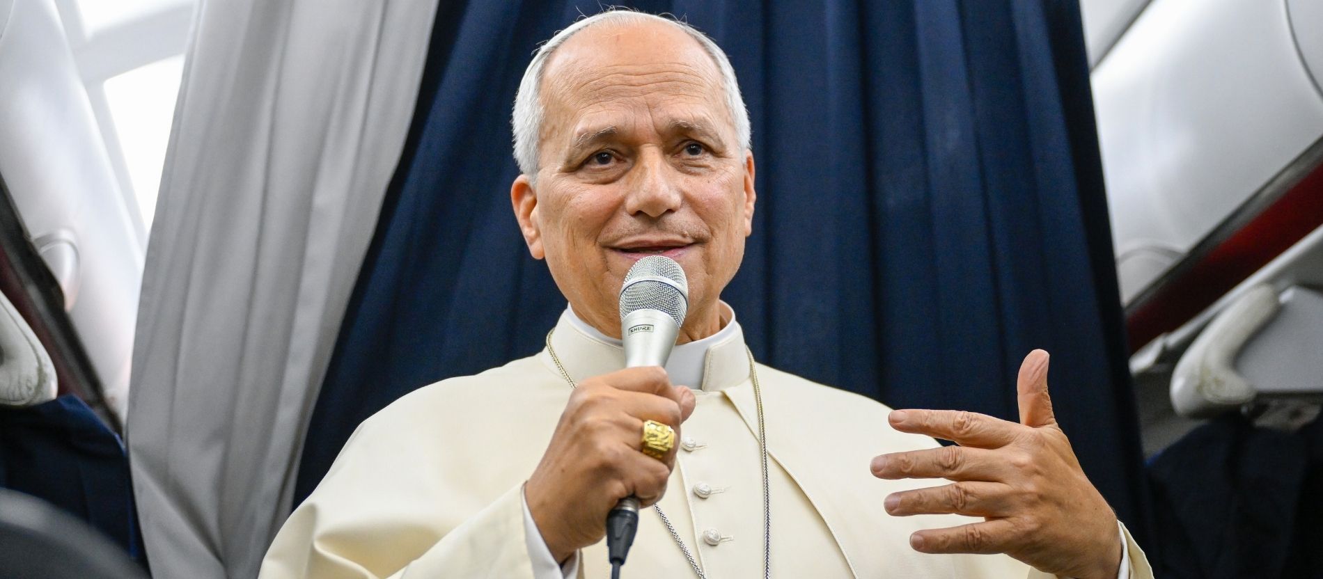 Papst Leo XIV. steht im Gang eines Flugzeugs und spricht in ein Mikrofon