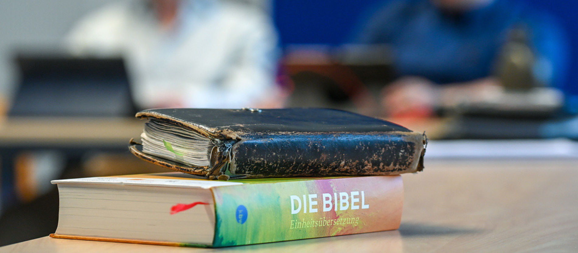 Eine Bibel und ein Notizbuch liegen gestapelt auf einem Tisch 