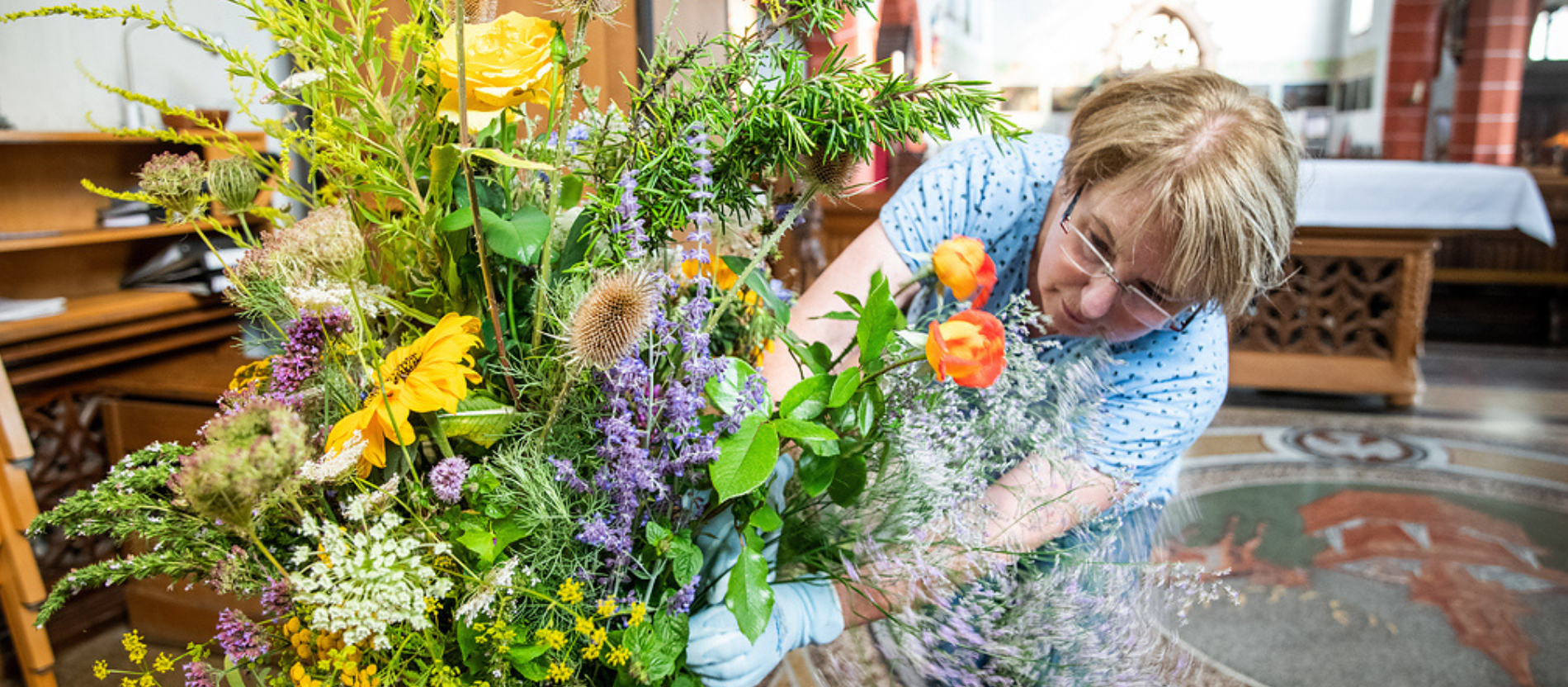 Eine Frau zupft einen großen Blumenstrauß zurecht aus gesammelten Kräutern und Wiesenblumen für einen Gottesdienst anlässlich von Mariä Himmelfahrt am 14. August 2021 in der Kräuterkirche in Bingen.