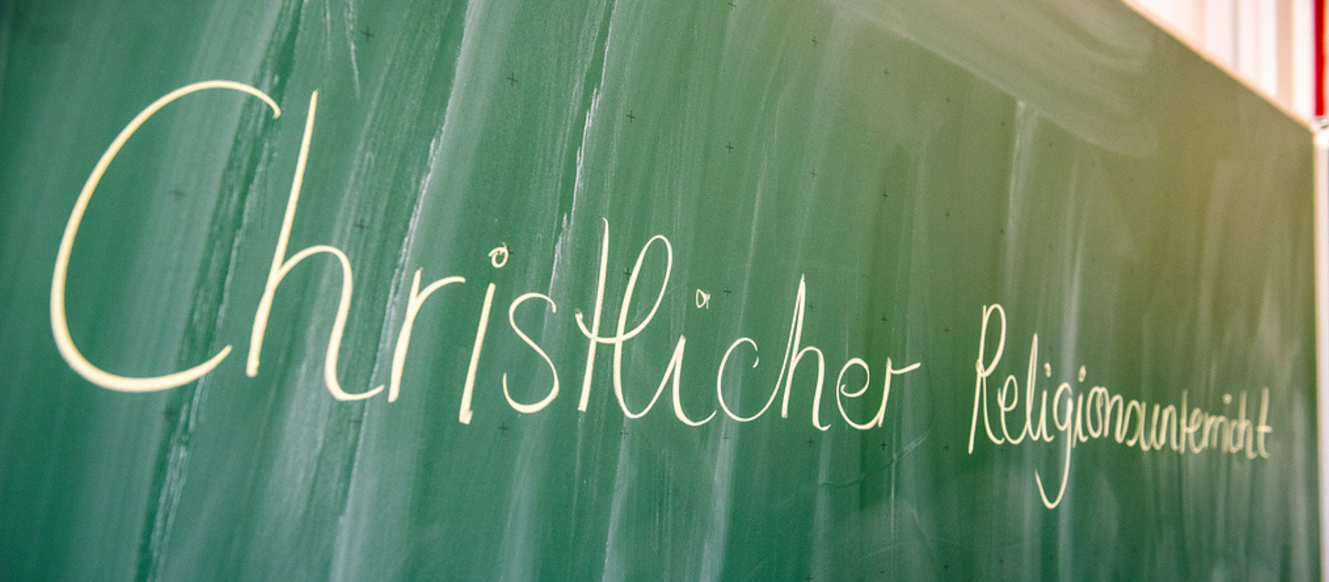 Schriftzug "Christlicher Religionsunterricht" in einem Klassenraum an einer Tafel.
