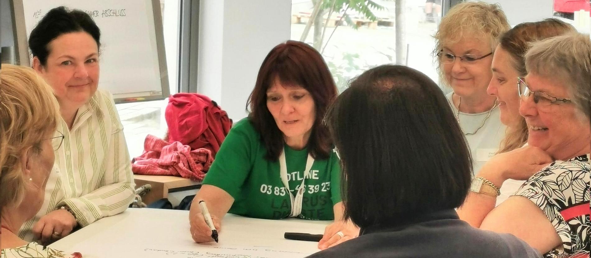 Martina Steinfurth sitz mit anderen Frauen an einem Tisch und schreibt etwas auf ein Flipchart-Papier. 
