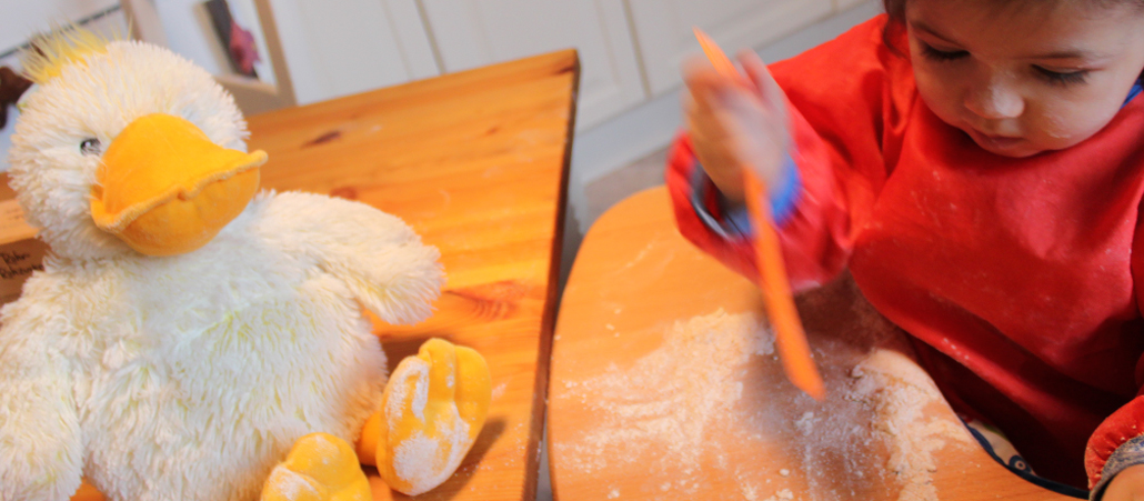 Kuschelente guckt einem Baby beim Spielen mit Mehl zu