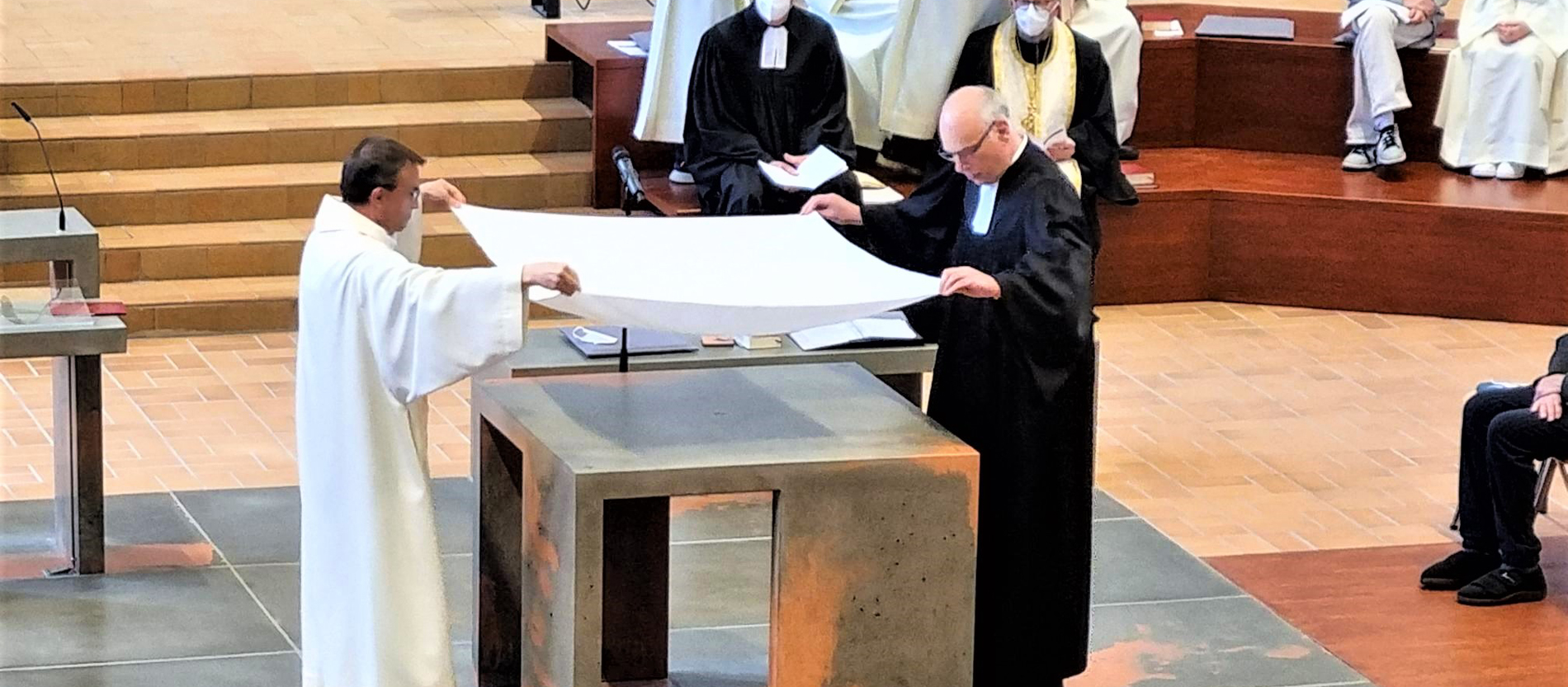 Ein katholischer und ein evangelischer Pfarrer breiten gemeinsam ein Altartuch aus