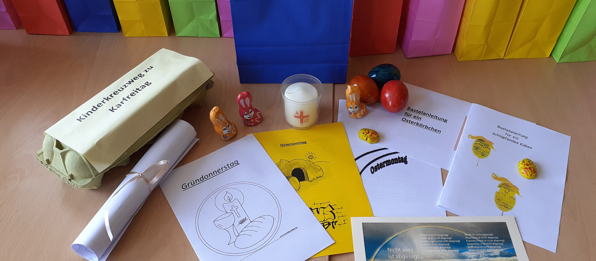 Auf einem Tisch liegen ein leerer Eierkarton, eine Osterkerze, Schokoladenhasen, Ostereier und Hefte mit spirituellen Impulsen und Bastelanleitungen.