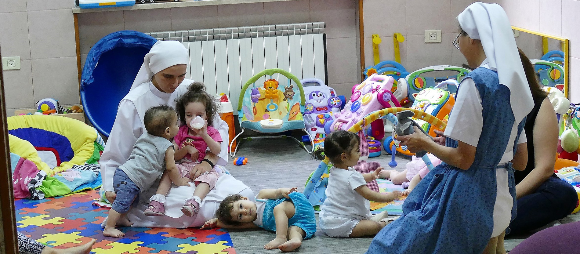 Kinder und Ordensschwestern in einem Raum mit Spielzeug.