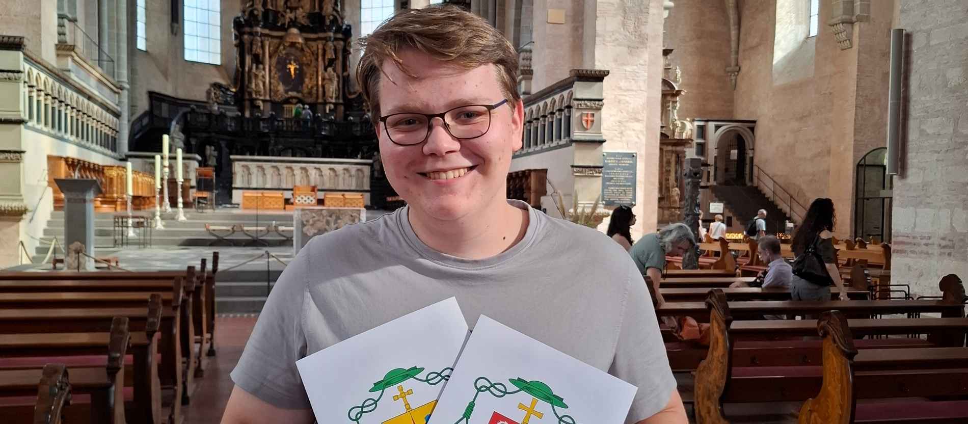 Lukas Böck mit zwei Abbildungen von Wappen in der Hand.