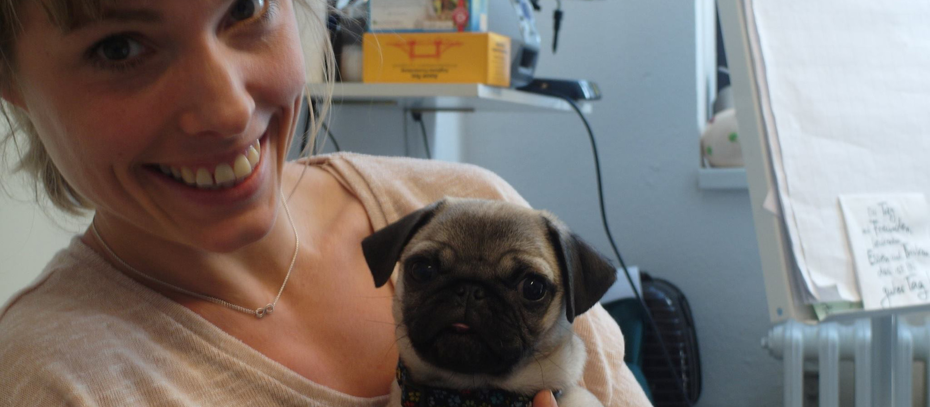 Eine lächelnde Frau hält einen Mops auf dem Arm.