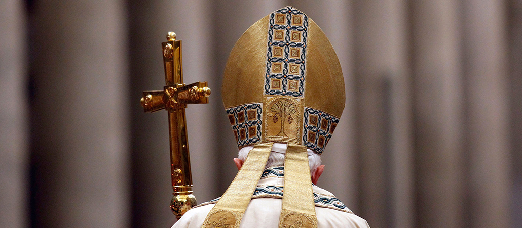 Bei der Mitra handelt es sich um die Kopfbedeckung für Papst, Bischöfe und Äbte. Sie ist spitz zulaufend und an der Rückseite mit zwei Zierbändern versehen. 
