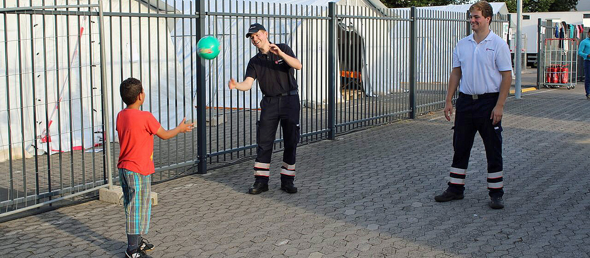 Zwei Malteser spielen mit einem Flüchtlingskind Ball.