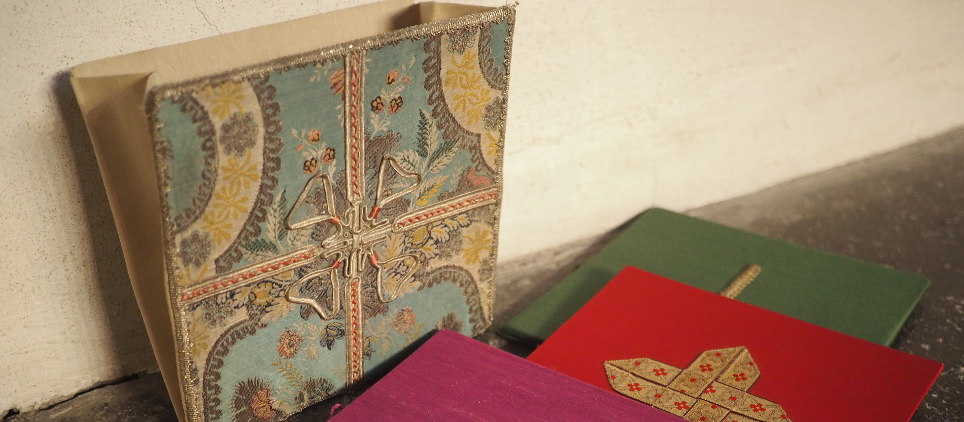 BURSA: Die Bursa ist eine kunstvoll bestickte Stofftasche aus zwei flachen, festen Teilen, in der das Korporale, also das Altartuch, aufbewahrt wird. Es passt in der Regel farblich zum Messgewand. Häufig ist ein Kreuz auf der Vorderseite eingestickt. Als Umhängetäschchen dient die Bursa auch zum Transport der Heiligen Kommunion und des Öls zur Krankensalbung bei Krankenbesuchen des Priesters. 
