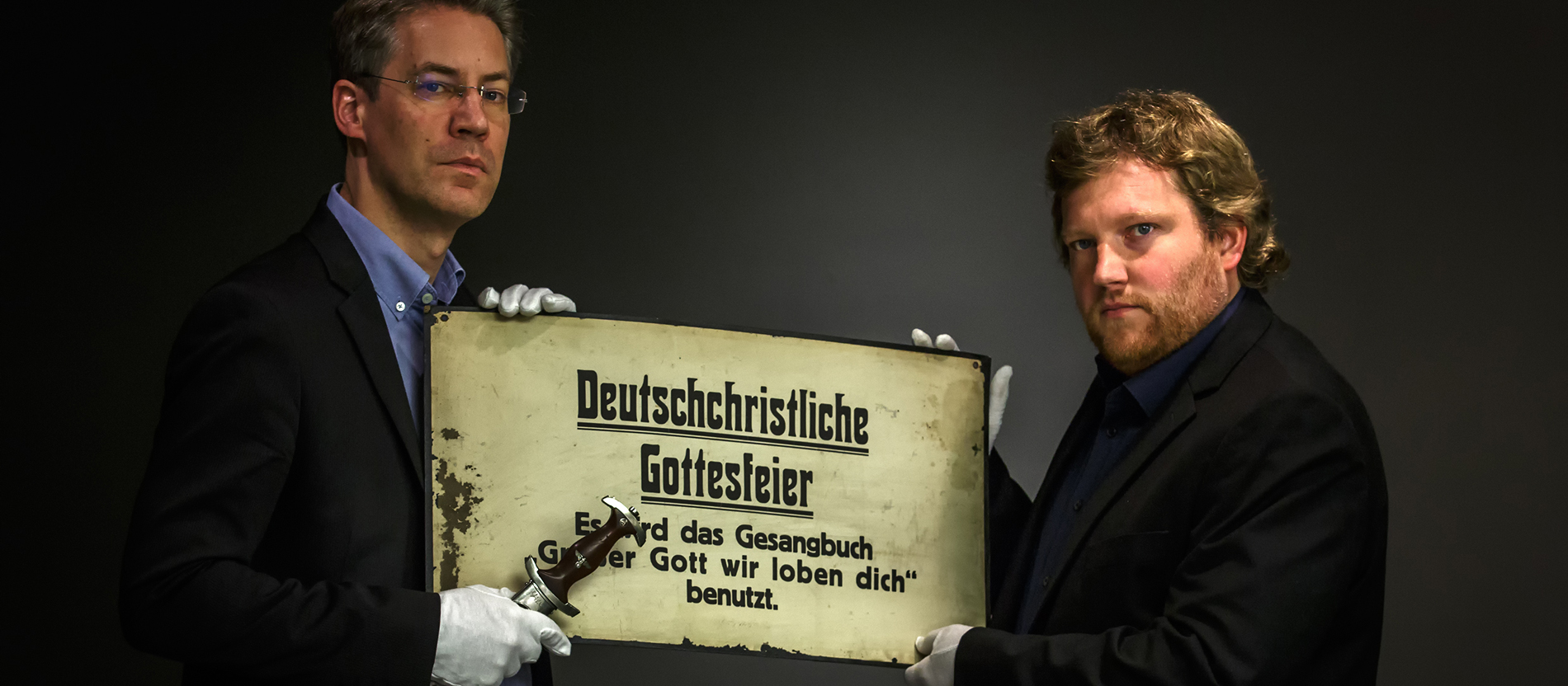 Zwei Menschen halten ein Plakat mit der Aufschrit deutschchristliche Gottesdienstfeier