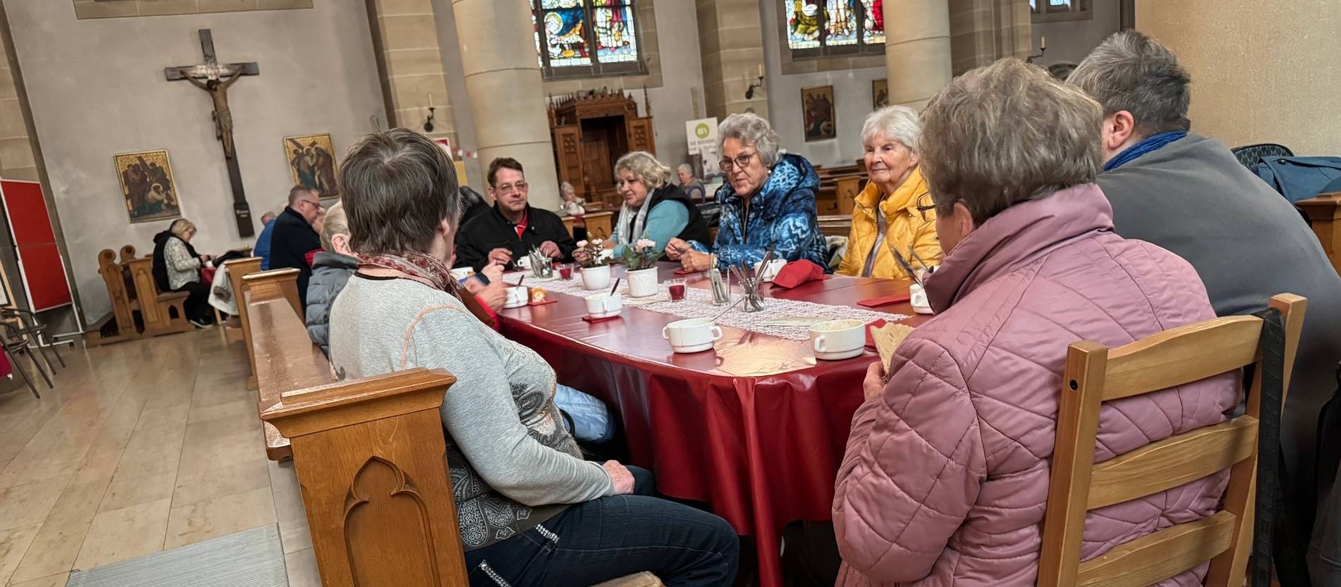 Gemeindemitglieder, Senioren, Ordensmänner und Obdachlose sitzen gemeinsam am Tisch. 