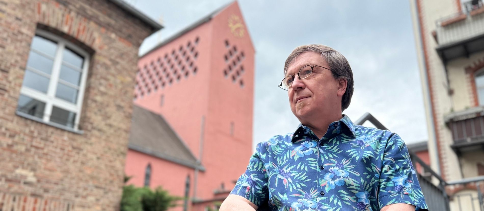 Stefan Diefenbach schaut an der Kamera vorbei, im Hintergrund ein Kirchturm