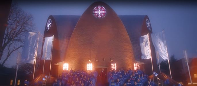 Screenshot aus dem Musikvideo "Facebook-Requiem" mit einer Frontansicht von St. Engelbert bei Nacht mit Chor