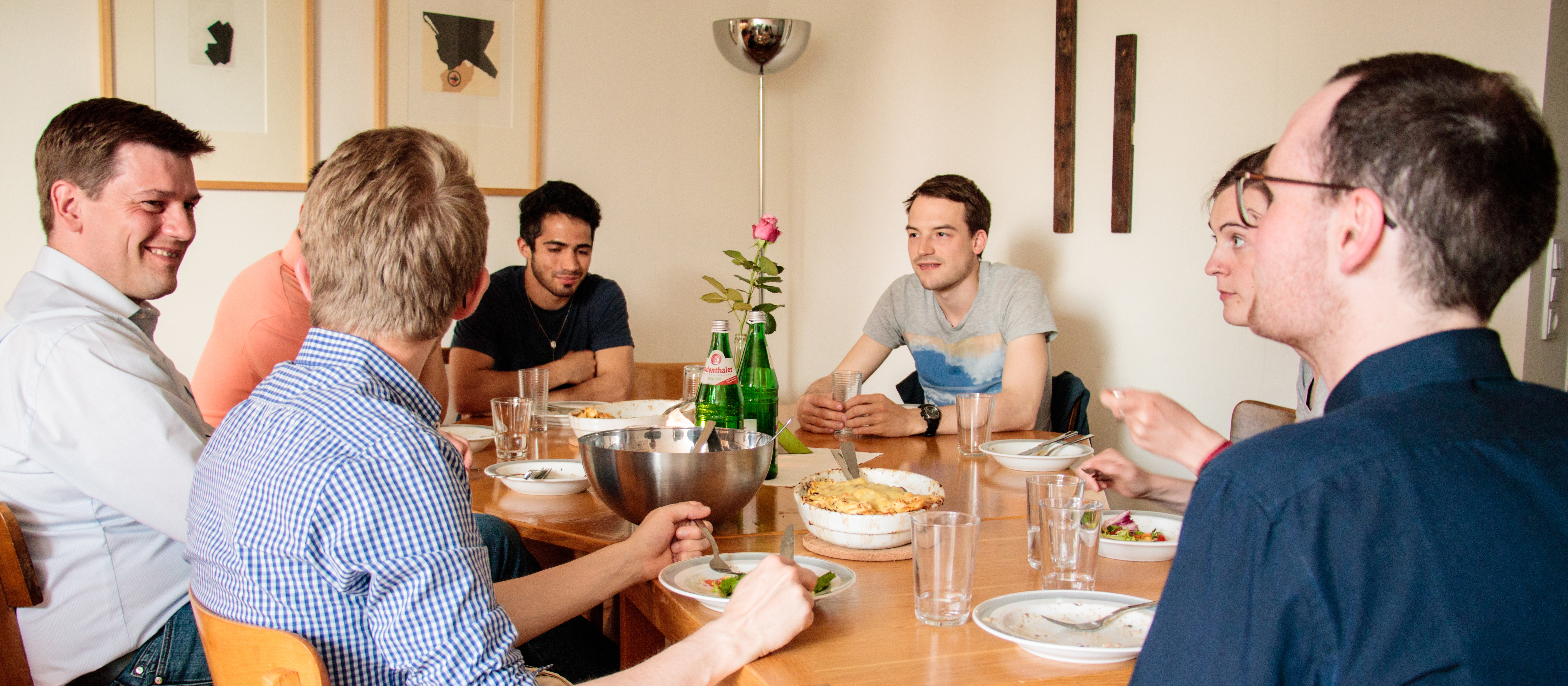 Mehrere junge Menschen sitzen am Esstisch und unterhalten sich.