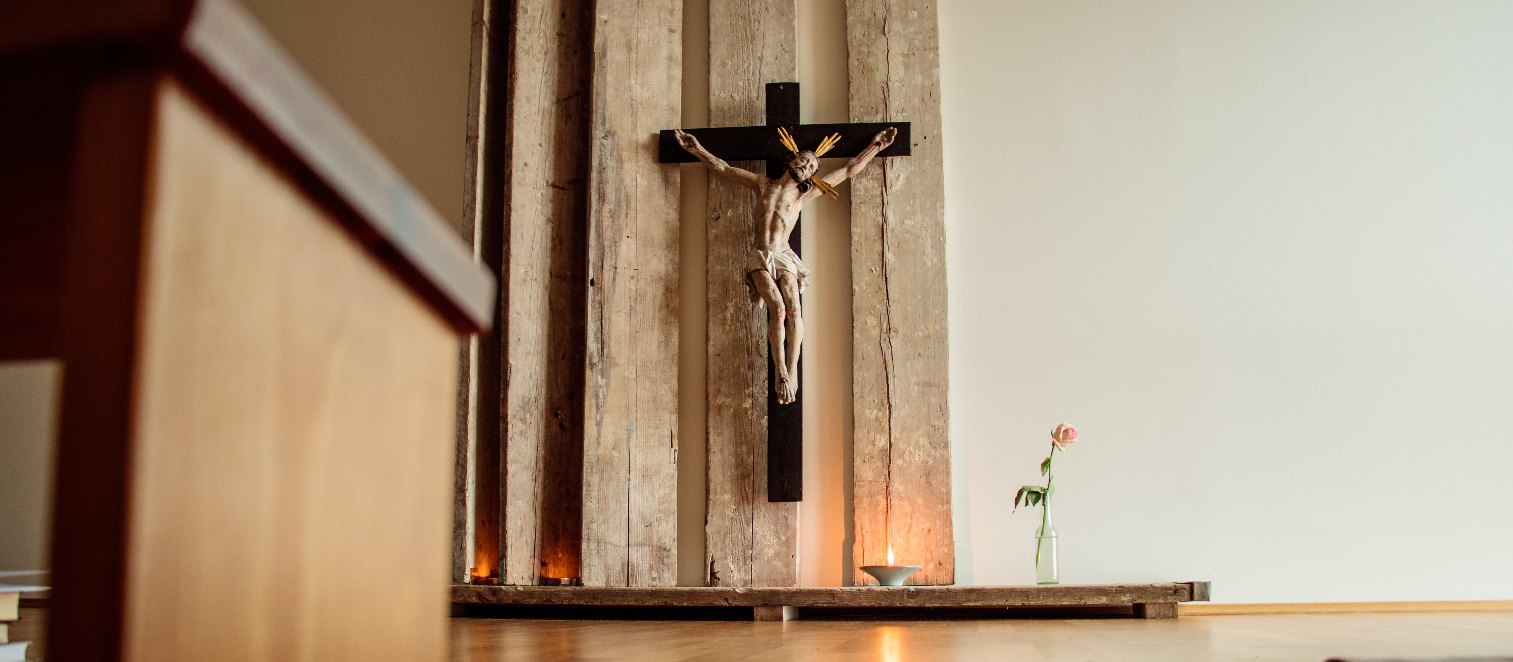 Im Vordergrund steht ein Gebetshocker, im Hintergrund ist ein Kreuz mit Corpus zu sehen.